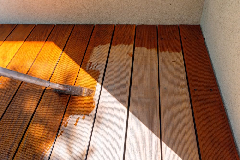 A deck staining pro brushing fresh stain into wood deck boards in Charlotte